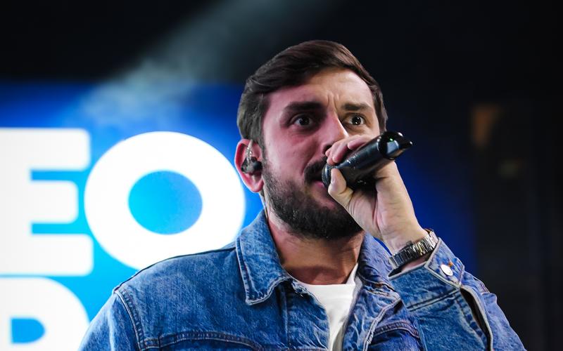 Leo Derobi cantando ao vivo no palco, com iluminação azul e público animado